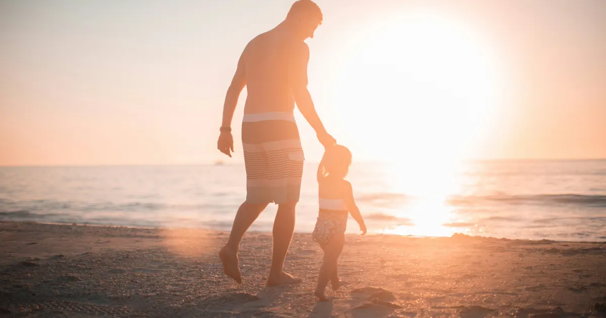 An adult and a small child walking hand in hand towards a low sun