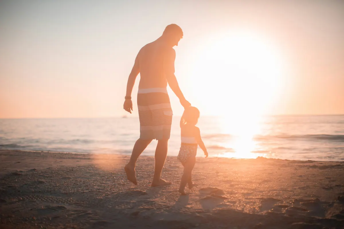 An adult and a small child walking hand in hand towards a low sun