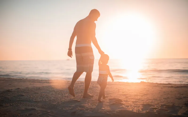 An adult and a small child walking hand in hand towards a low sun