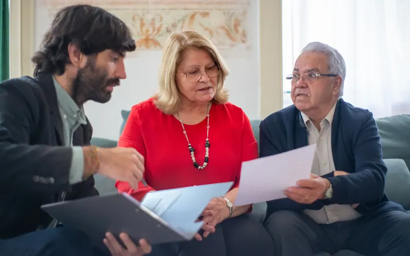 A younger man showing a tablet to an older couple seated together on a sofa
