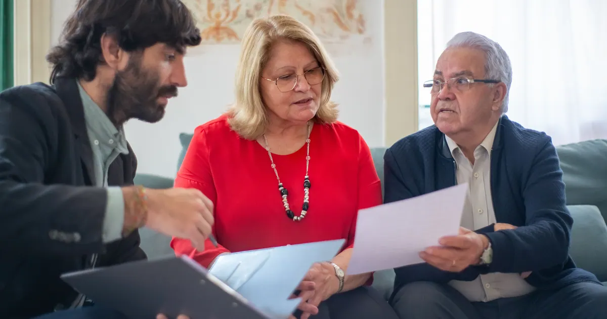 A younger man showing a tablet to an older couple seated together on a sofa