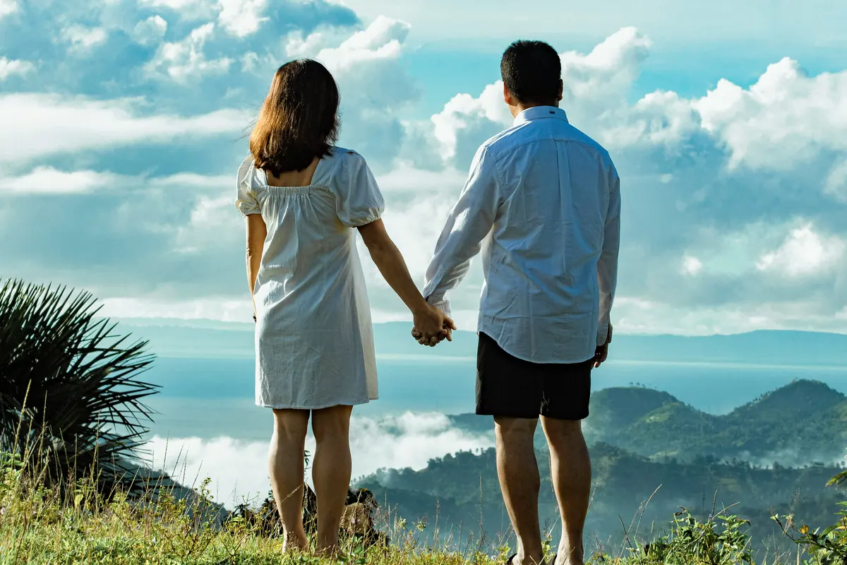 A couple standing hand in hand on a hillside, looking out towards distant mountains
