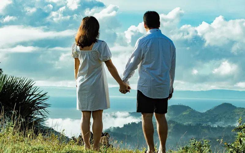 A couple standing hand in hand on a hillside, looking out towards distant mountains