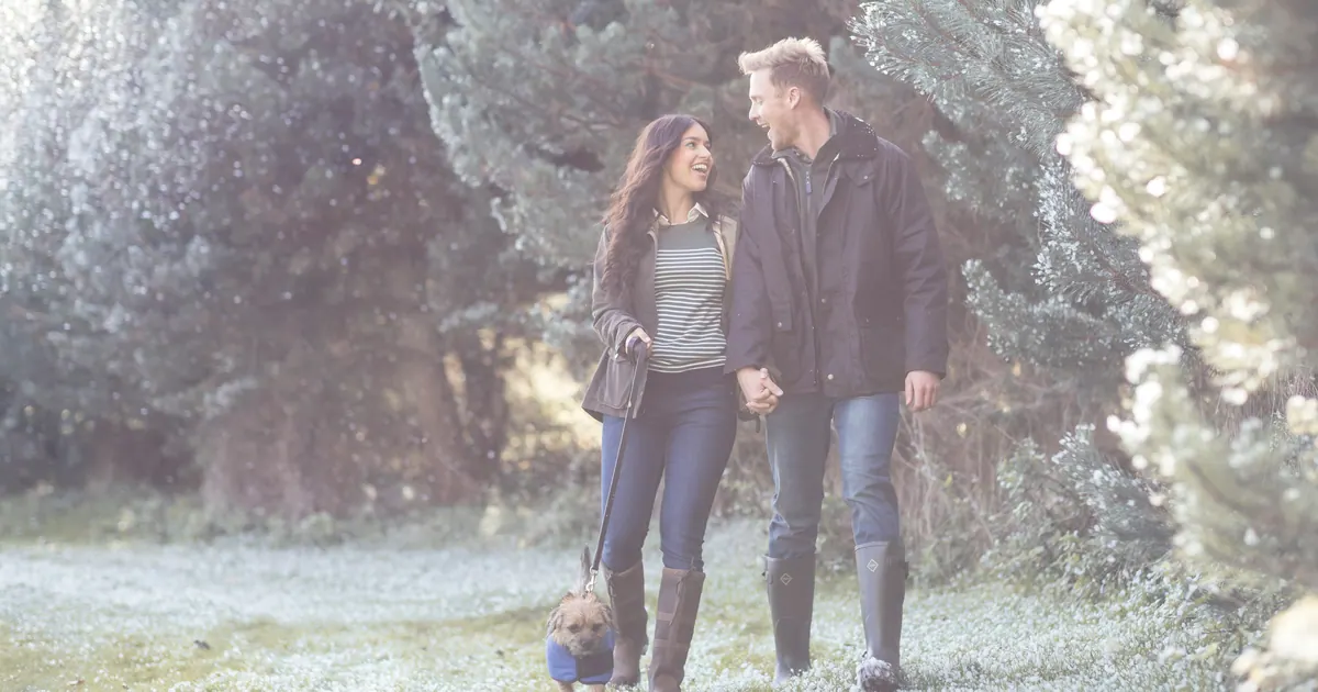 A couple walking a dog together across a frosted field in winter light