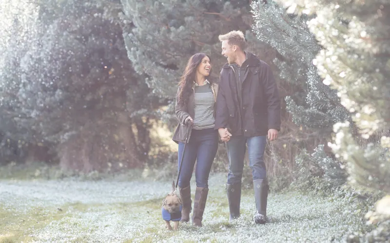 A couple walking a dog together across a frosted field in winter light