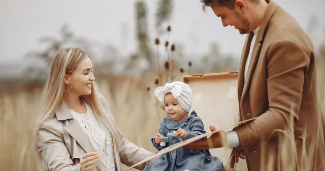 Two parents and a baby sitting together in an autumn field