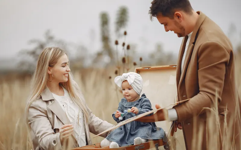 Two parents sitting with their baby between them in an autumn field