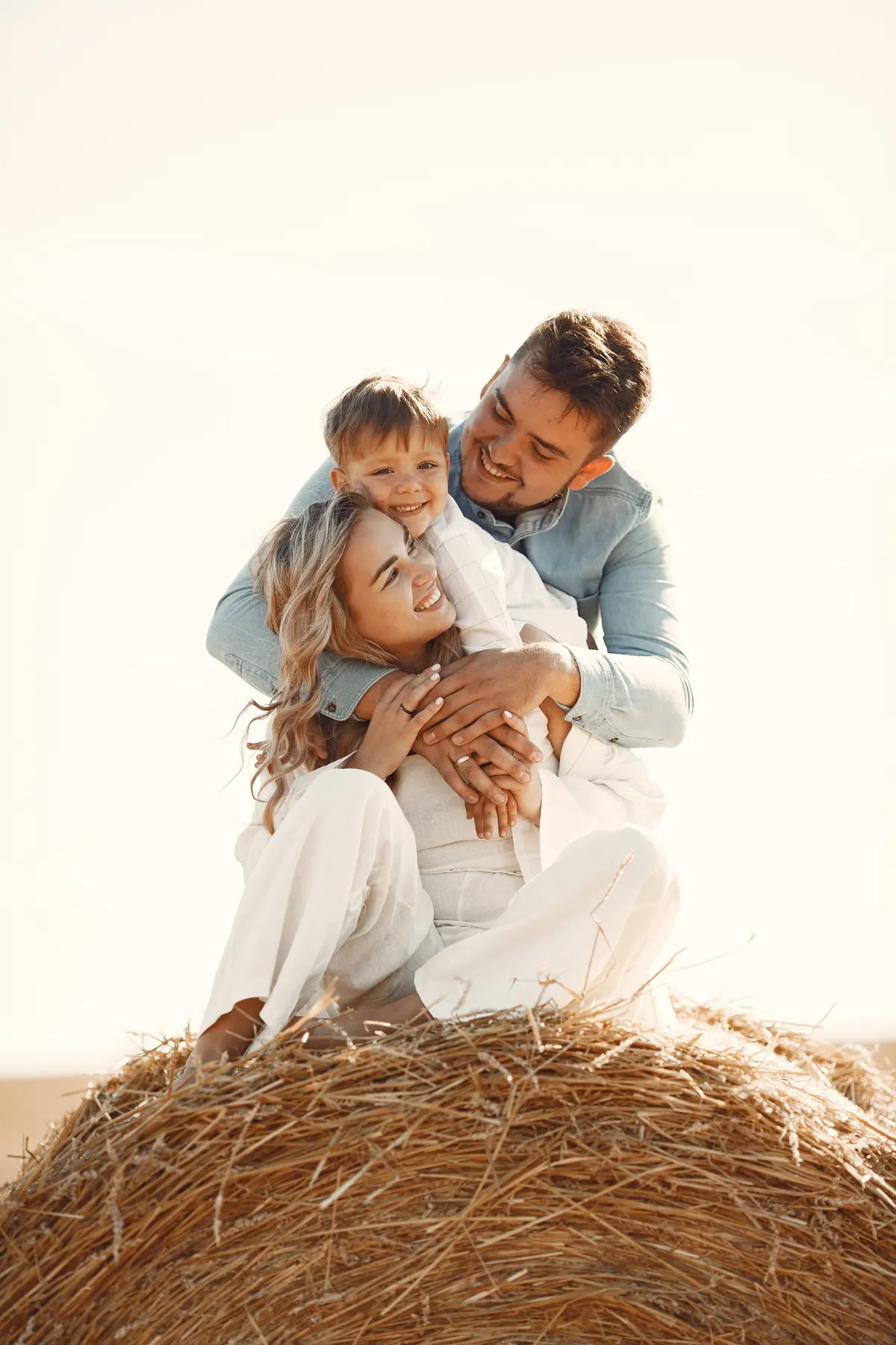 A family holding each other closely while sitting on a round hay bale