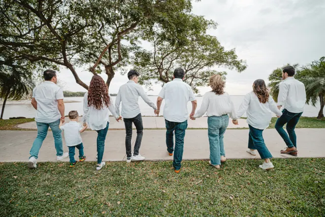 An extended family holding hands in a line, walking together towards open water, seen from behind
