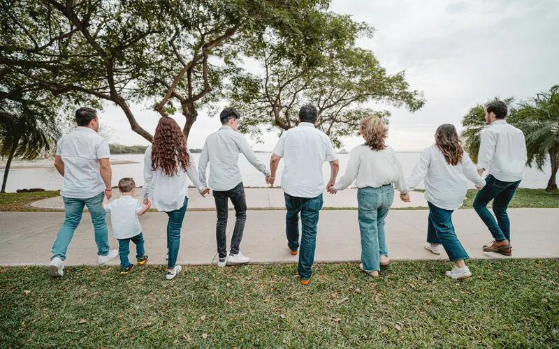 An extended family holding hands in a line, walking together towards open water, seen from behind