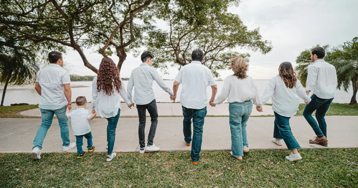 An extended family holding hands in a line, walking together towards open water, seen from behind