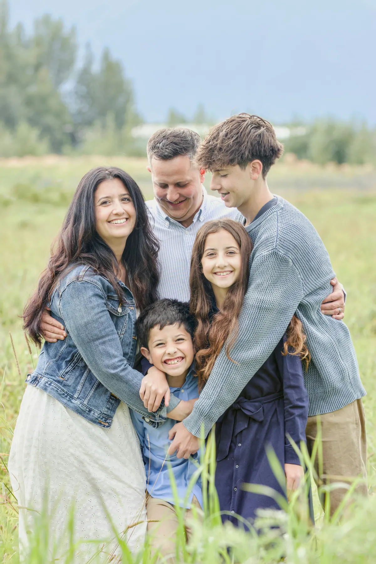 A family of five standing together in tall grass with their arms around each other