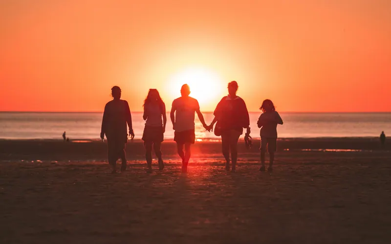 A family of five walking along a shoreline at sunset, seen in silhouette