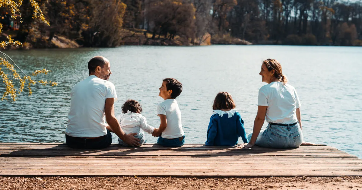 A family of five sitting along a wooden jetty looking out over a lake