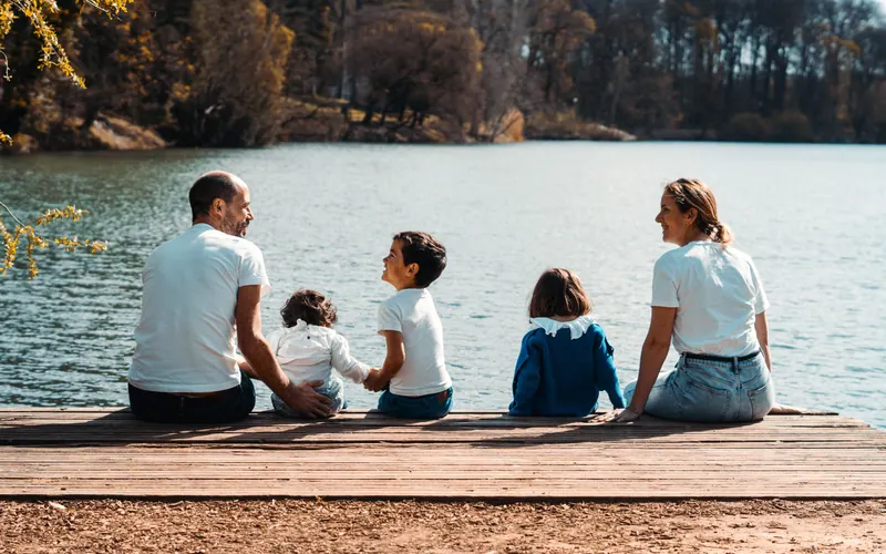 A family of five sitting along a wooden jetty looking out over a lake