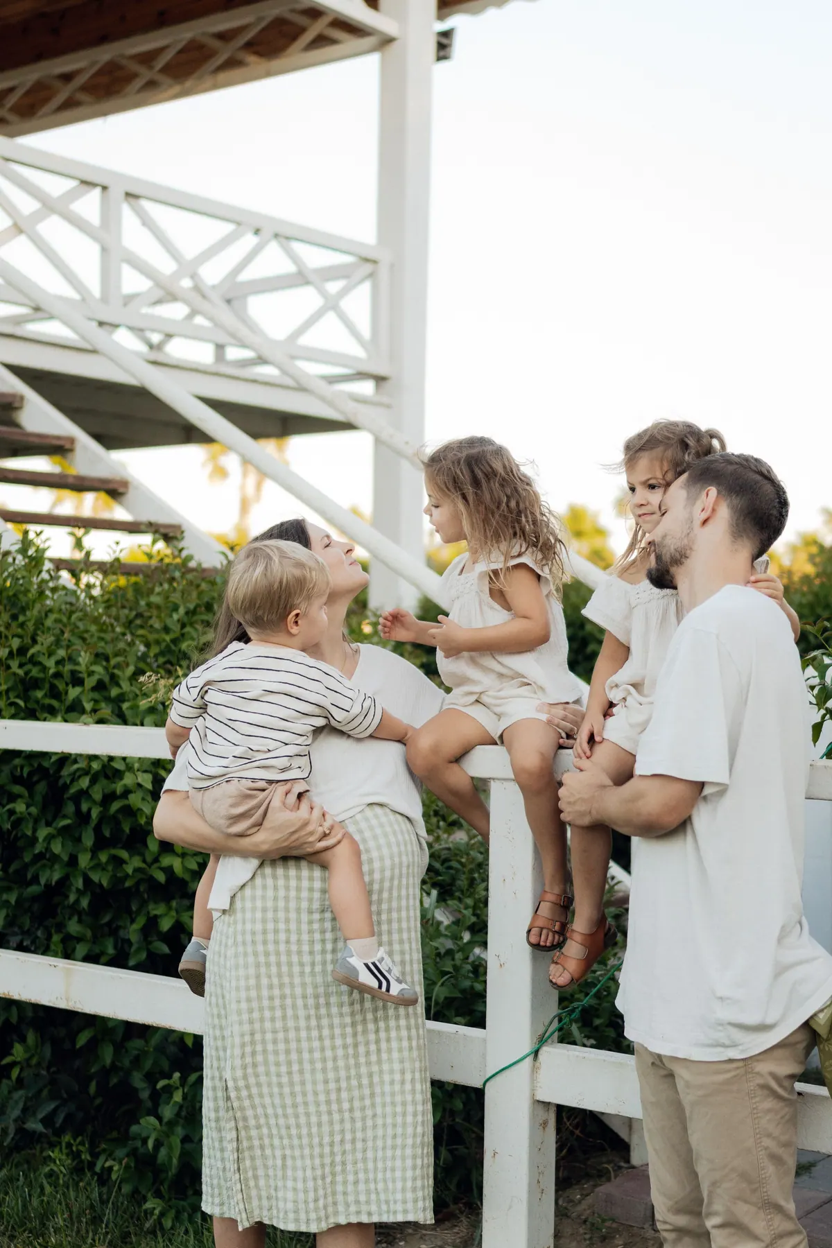 A family of four gathered by a white porch railing, the mother holding a small boy