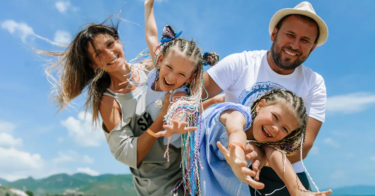 A family of four laughing together outdoors with the wind in their hair