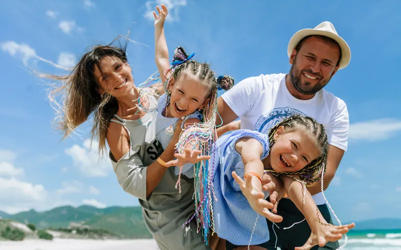A family of four laughing together outdoors with the wind in their hair