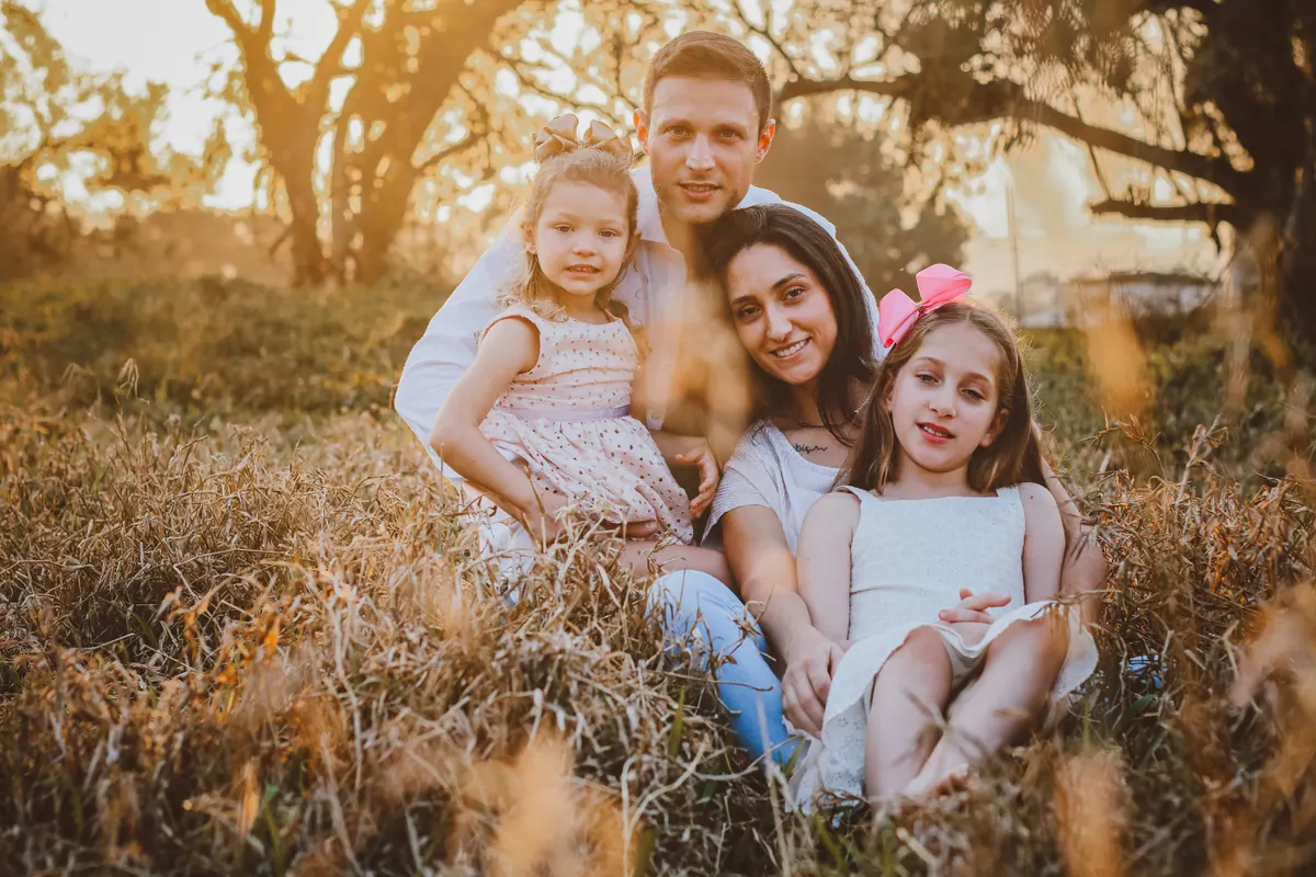 Two parents and two young girls sitting together in dry golden grass in late afternoon light