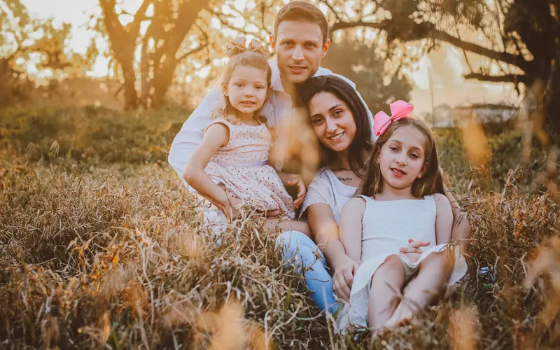 Two parents and two young girls sitting together in dry golden grass in late afternoon light