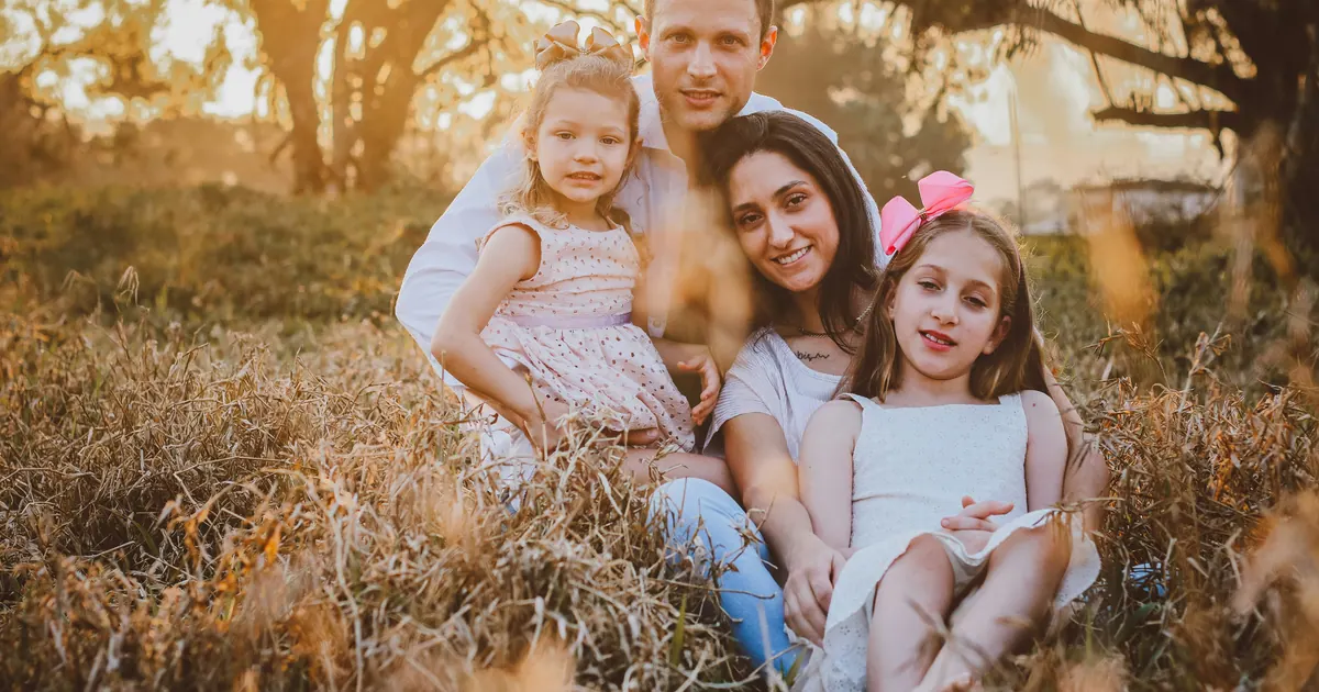 Two parents and two young girls sitting together in dry golden grass in late afternoon light