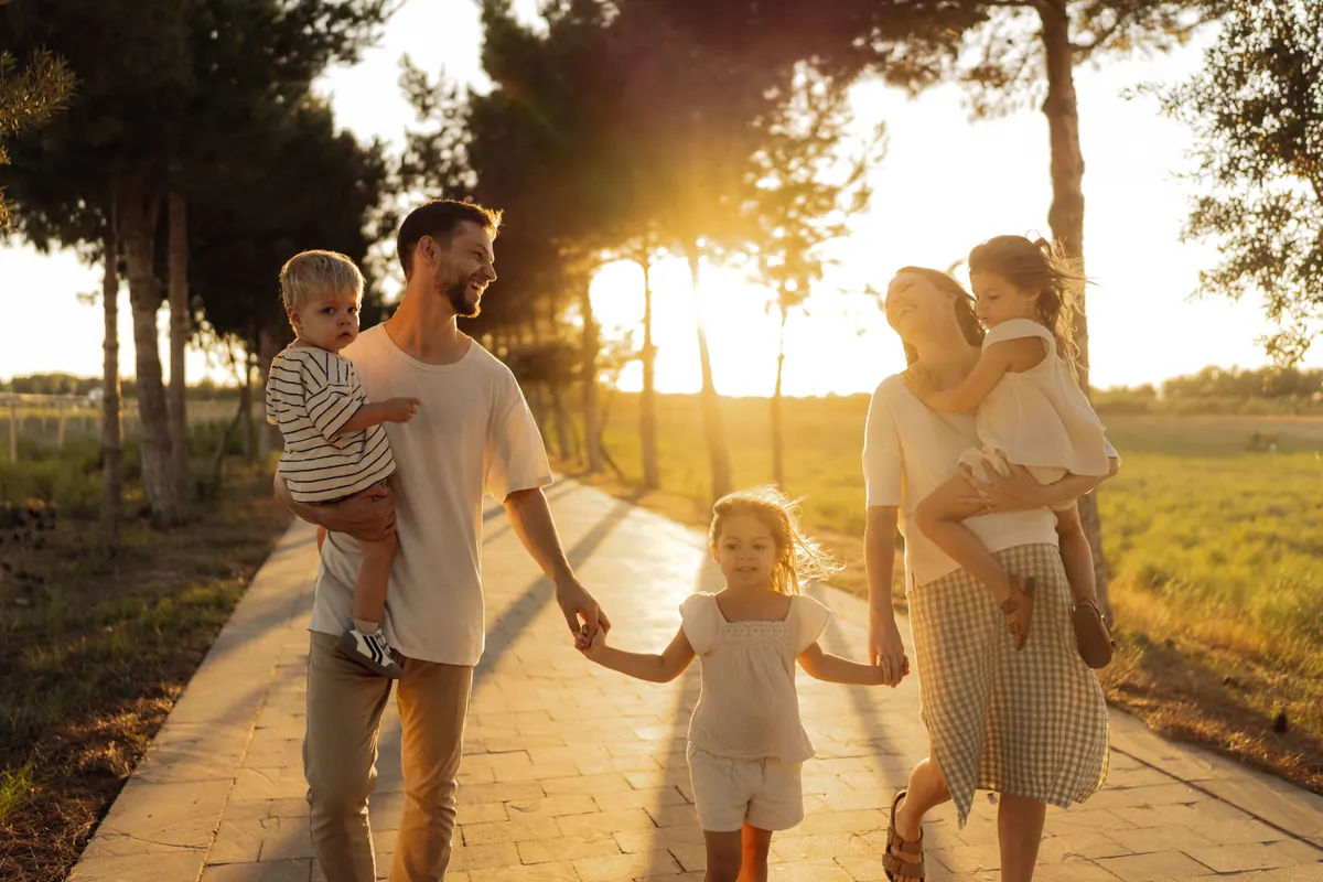 A family of four walking hand in hand along a path towards the camera at sunset