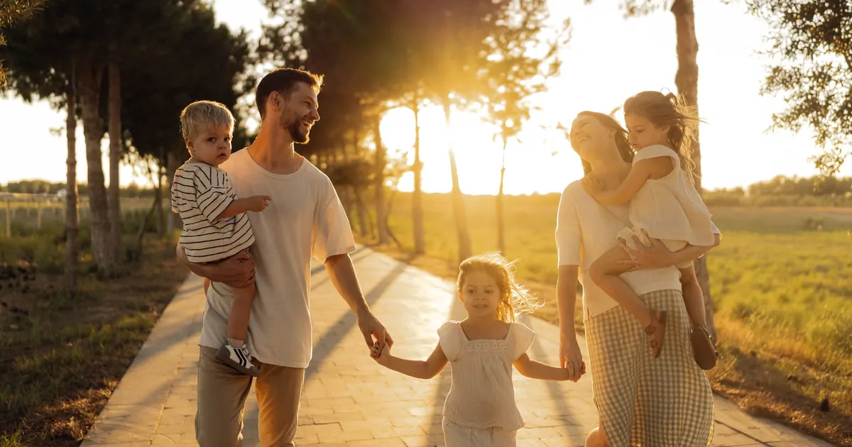 A family of four walking hand in hand along a path towards the camera at sunset