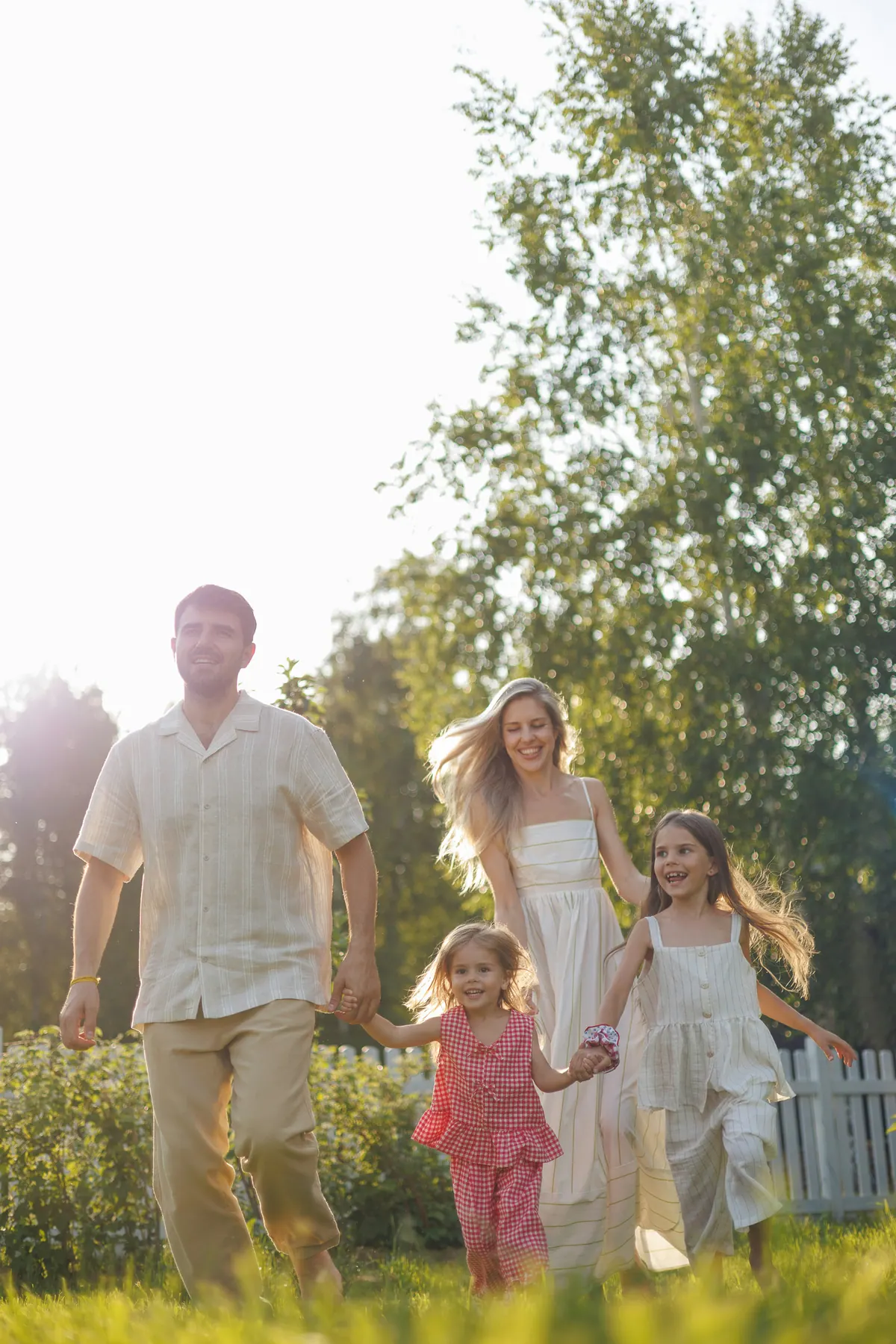 A family of four walking hand in hand across a lawn towards the camera