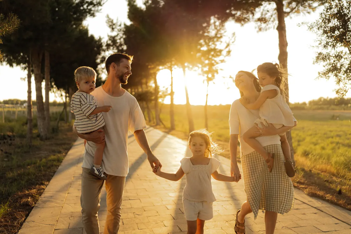 A family of four walking hand in hand along a tree lined path towards the setting sun