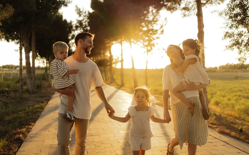 A family of four walking hand in hand along a tree lined path towards the setting sun