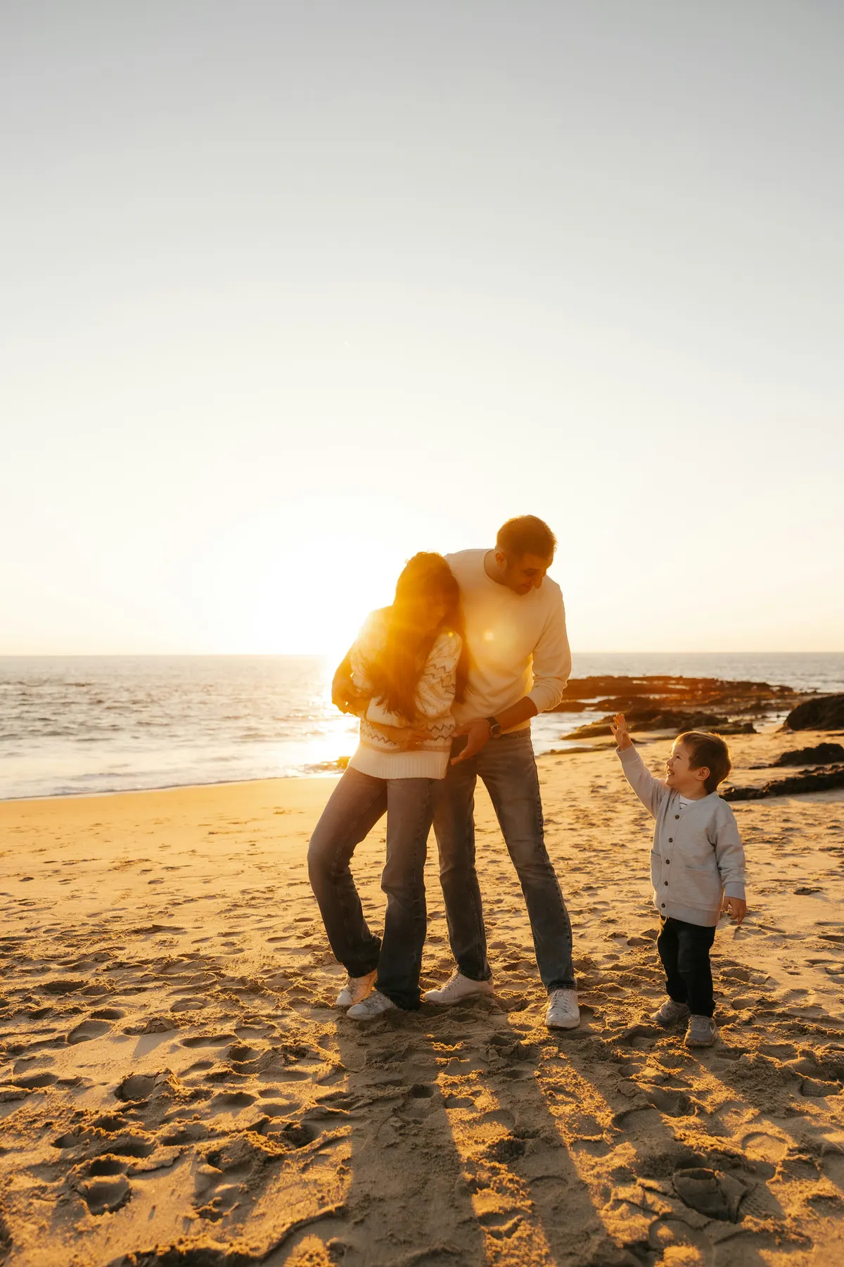 Two parents standing close together on an evening beach with a small child beside them