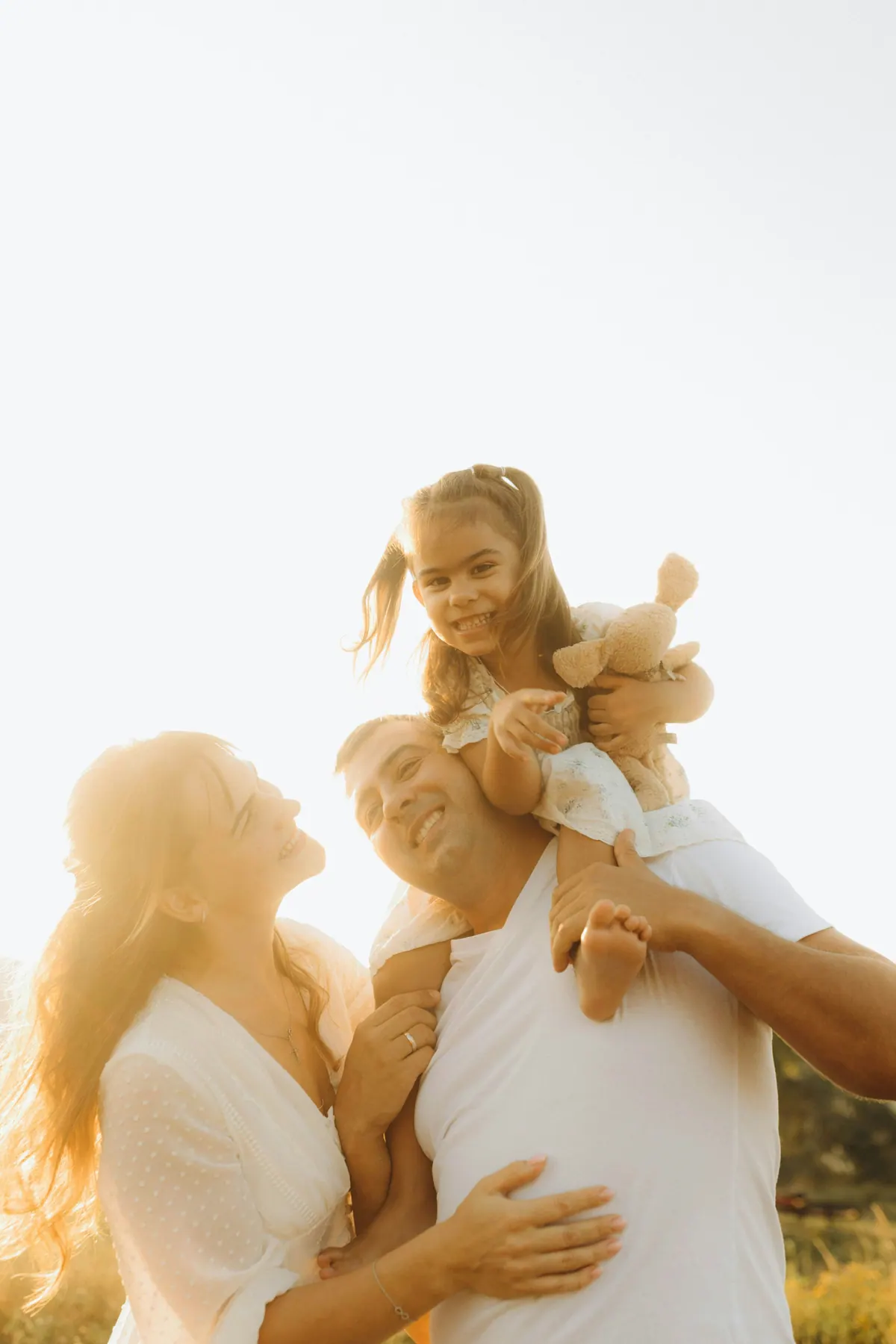 A girl sitting on her father's shoulders with her mother laughing beside them