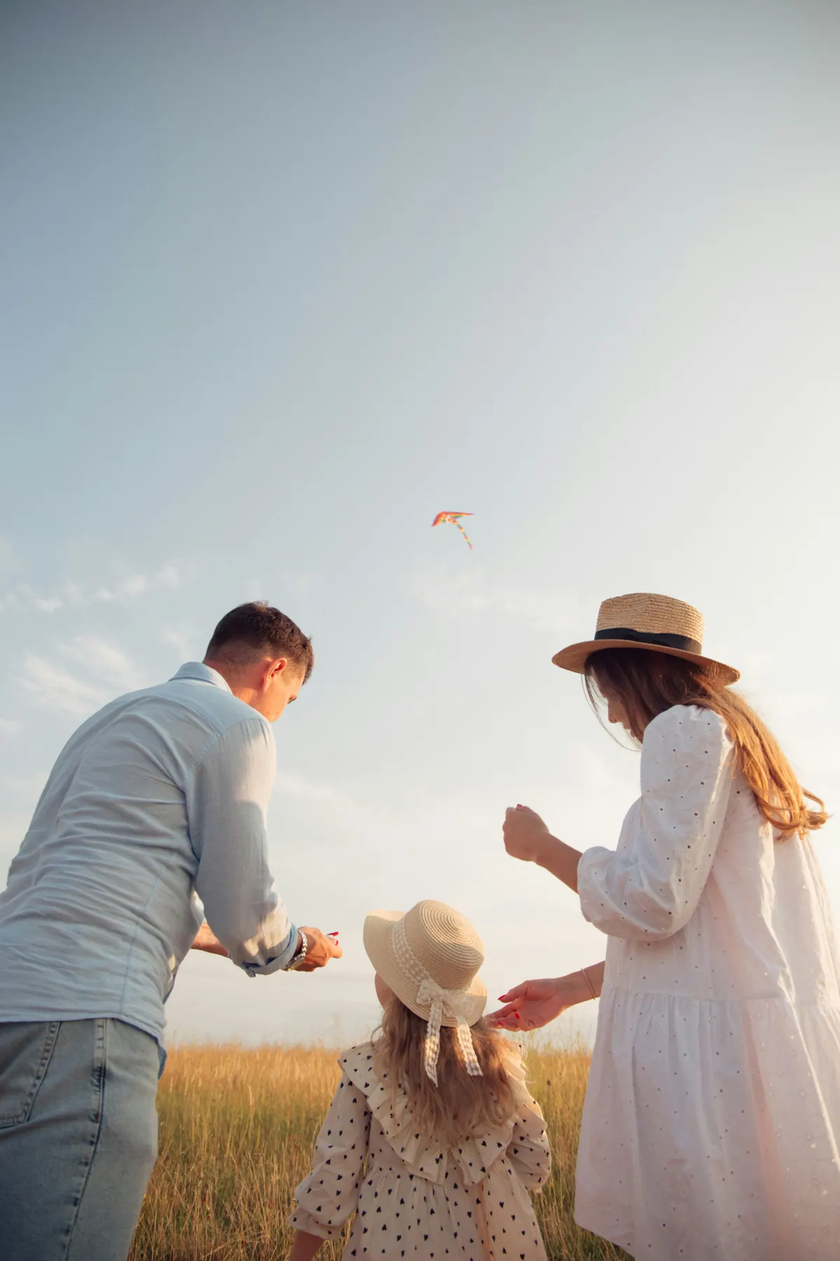 Two parents and a child flying a kite in a wheat field, seen from behind
