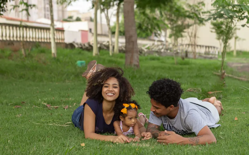 A family lying together on the grass in a park, a baby between the two parents