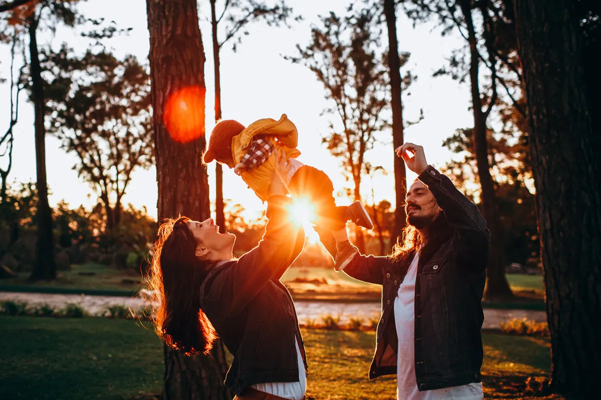 A family playing together among pine trees with low sun flaring through the branches
