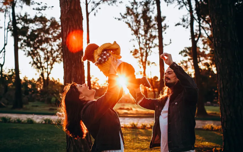 A family playing together among pine trees with low sun flaring through the branches
