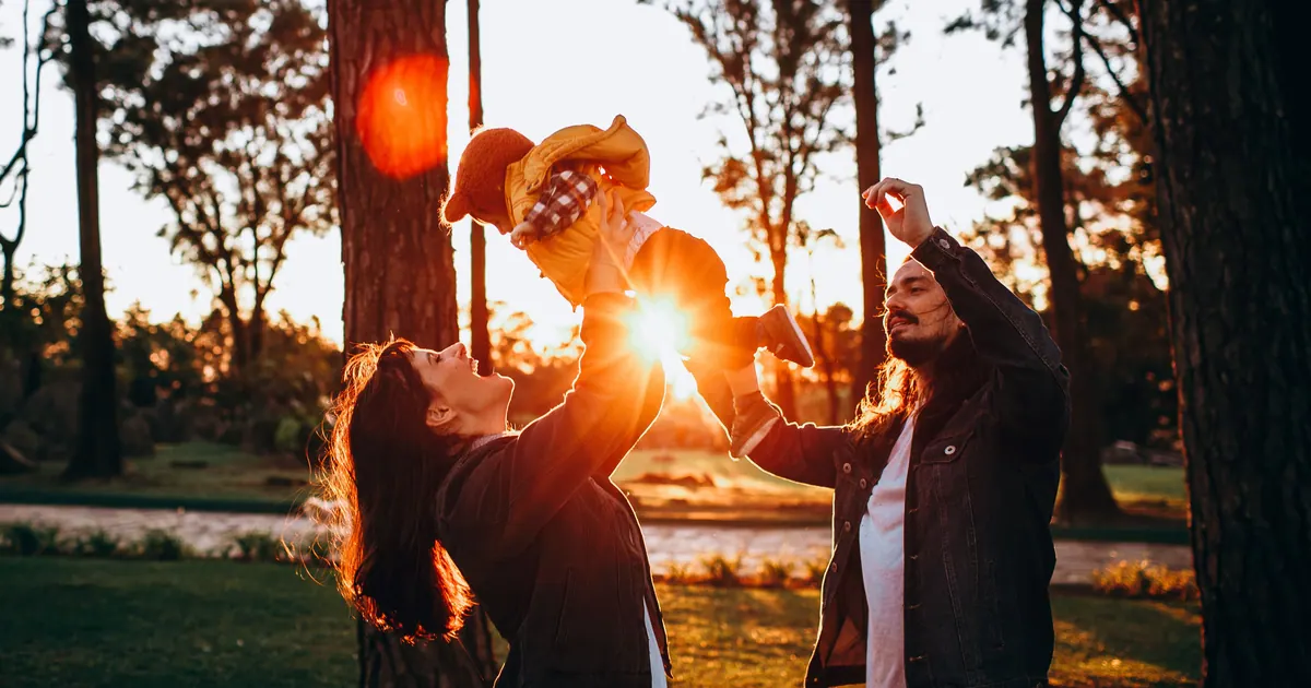 A family playing together among pine trees with low sun flaring through the branches