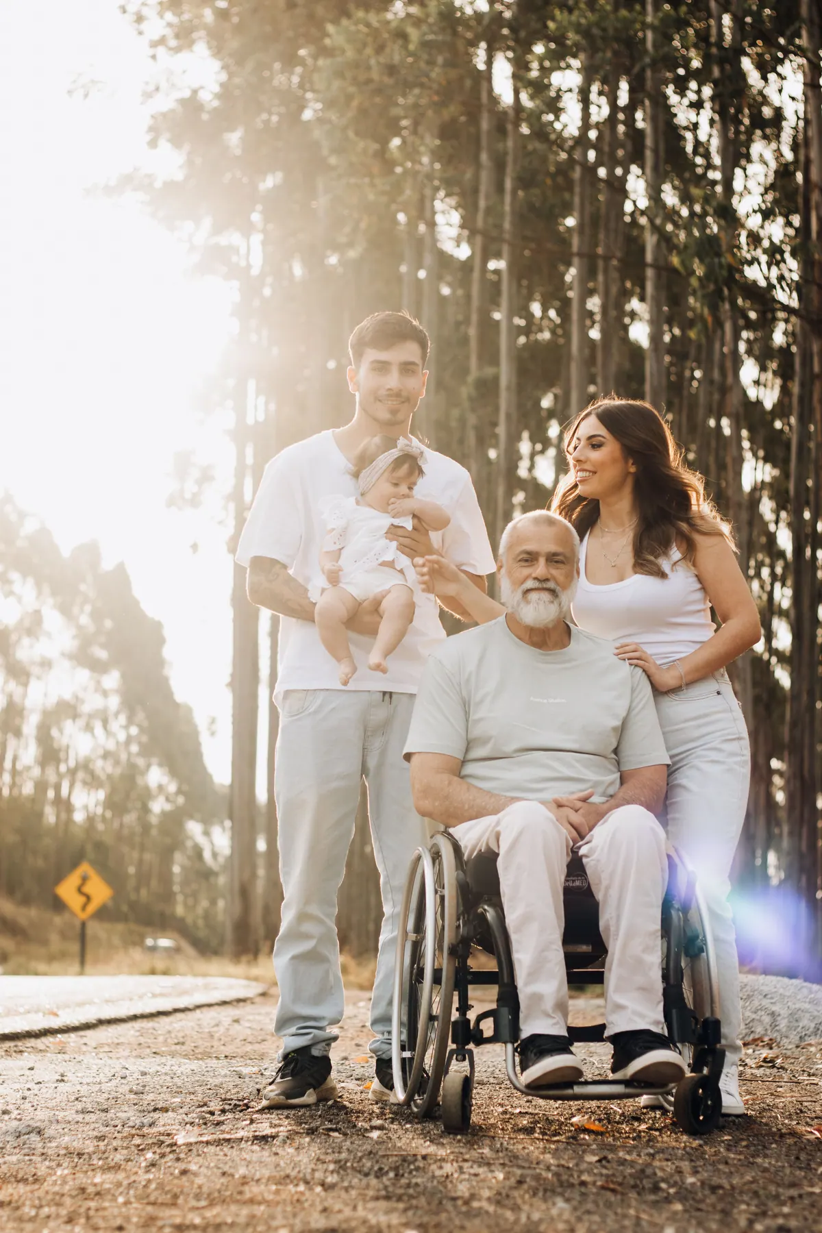 A family standing together on a forest road with an older man seated in a wheelchair among them