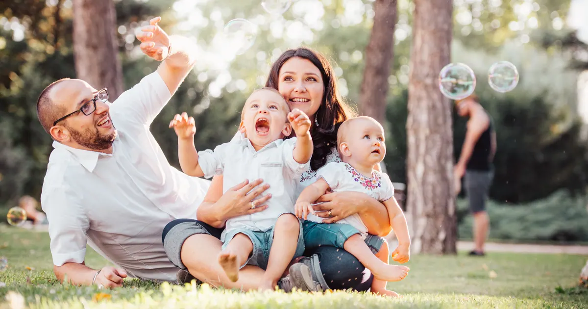 Two parents and three children sitting together on grass among pine trees