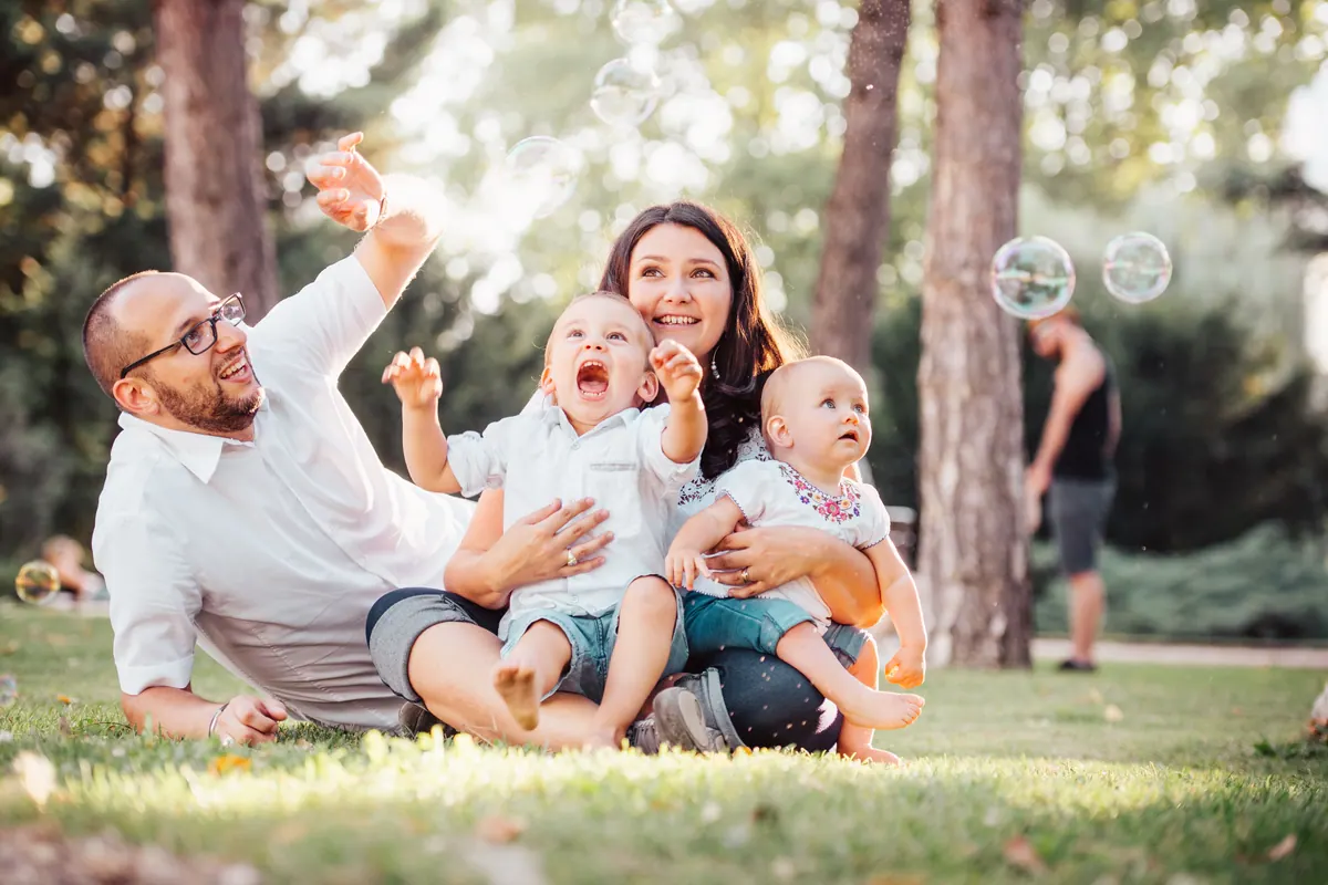 Two parents and three children sitting together on grass among pine trees