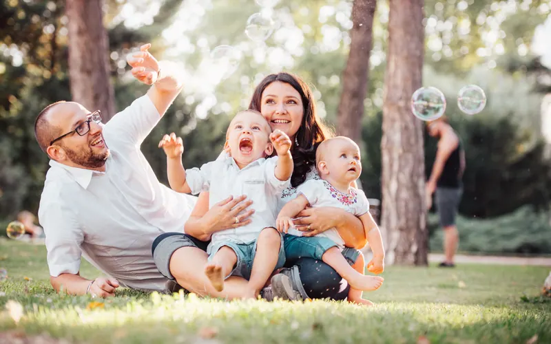 Two parents and three children sitting together on grass among pine trees