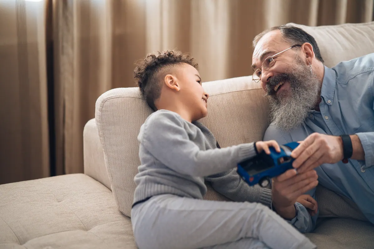 An older man and a young boy playing with a toy car on a sofa