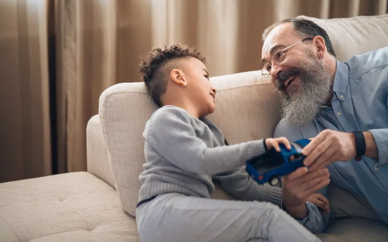 An older man and a young boy playing with a toy car on a sofa