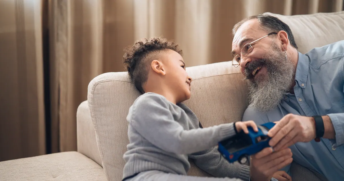 An older man and a young boy playing with a toy car on a sofa