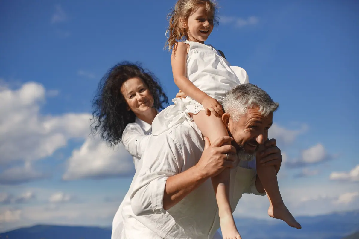An older man carrying a young girl on his back against an open blue sky