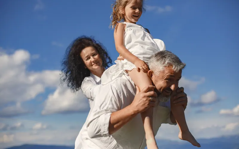 An older man carrying a young girl on his back against an open blue sky