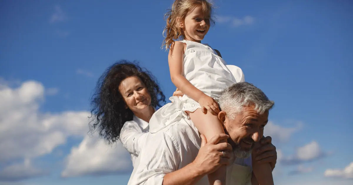 An older man carrying a young girl on his back against an open blue sky