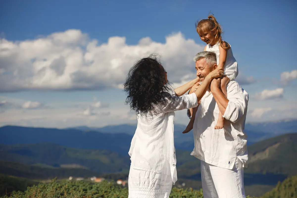 An older couple with a young girl on the man's shoulders, mountains and cloud behind them