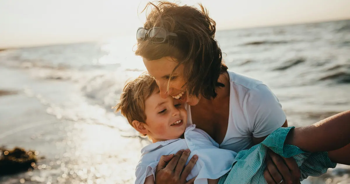 A mother holding a young child close at the edge of the water