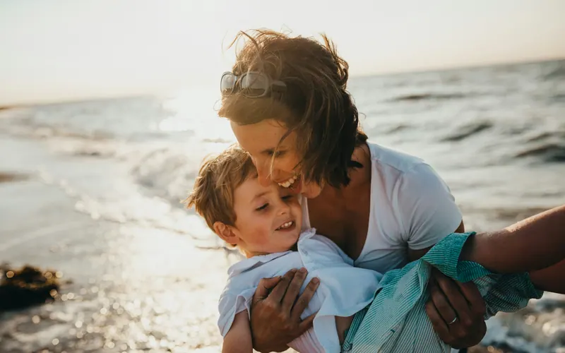 A mother holding a young child close at the edge of the water